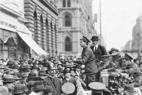 A large crowd of spectators in Collins Street during the Conscription Referendum campaign listen to soldiers addressing the gathering from a dais.