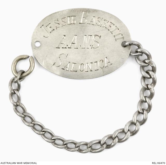 Identity bracelet worn by Staff Nurse Jessie Bassetti. It has an oval metal disc with her details engraved on it with a silver chain.