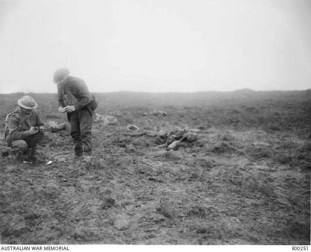Two soldiers in a muddy landscape looking at objects collected from the battlefield.