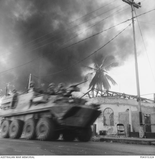"Dili burns as An Australian Armoured Personnel Carrier (APC) drives through a Dili street on patrol, past burning buildings set ablaze by either the Indonesian military or the pro-Indonesian militia."