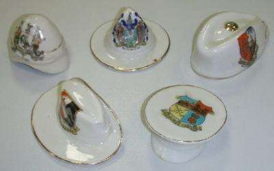 A collection of crested china military hats, including a pith helmet,; a ‘lemon squeezer’ hat, Glengarry cap,Australian slouch hat, and peaked cap.