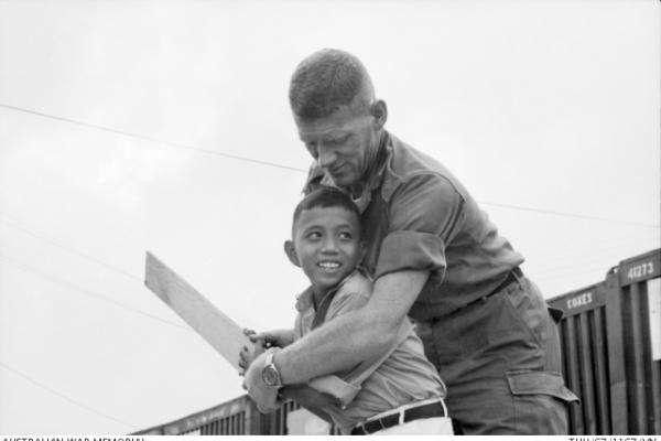 Vietnam War: Lieutenant Stevenson instructs Hue, a young Vietnamese boy, in holding a plank of wood as a cricket bat. Hue's Viet Cong parents were killed just three months earlier.