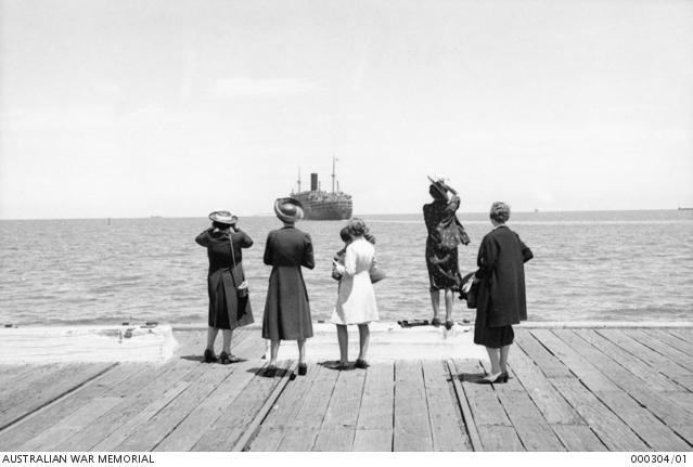 As a troopship sails in Port Phillip Bay in December 1939 a small group of women wave farewell from the wharf.
