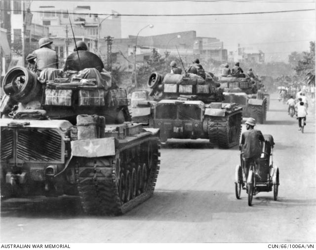 A pedi-cab operator in Saigon is dwarfed by a huge convoy of American Army tanks moving through the city streets.