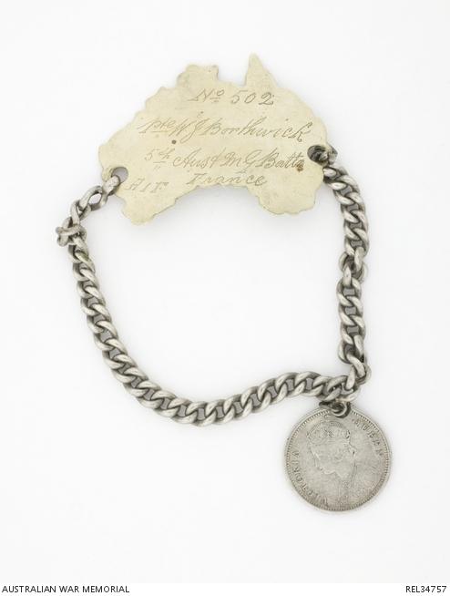 Identity bracelet  worn by Wilfred James Borthwick. The metal disc is carved in the shape of the map of Australia and has the soldier’s details engraved on it. It is attached to a chain, which has an Indian coin hanging off it.
