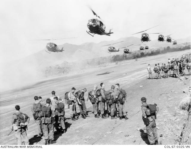 "Troops from 7th Battalion, The Royal Australian Regiment (7RAR), wait at Luscombe Field, while mates are lifted off by a fleet of Iroquois helicopters."