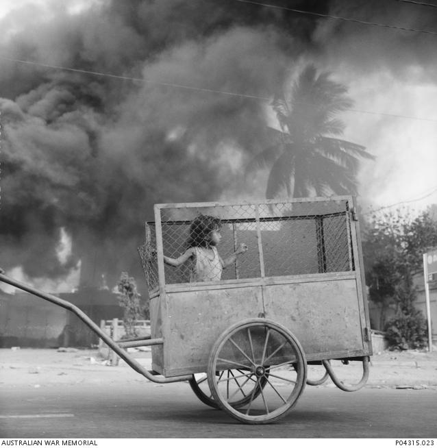 "Stephen Dupont, Dili burns behind a small child in a cart, 1999 P04315.023"