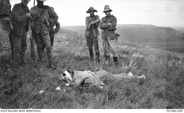 "Herbert Appleby, A wounded Boer soldier lies face down on the ground with his head bandaged as members of the 5th Contingent, Victorian Mounted Rifles, look on, January 1902 P01866.009"