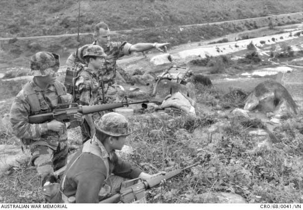 QUANG TRI PROVINCE. SOUTH VIETNAM. 1968-01. AUSTRALIAN ARMY ADVISER CAPTAIN PETER REID OF SYLVANIA WATERS, NSW (REAR RIGHT), SPEAKS WITH HIS SOUTH VIETNAMESE RADIO OPERATOR NEAR THE SA HUYNH FORWARD OBSERVATION BASE IN QUANG TRI PROVINCE. CAPTAIN REID, A