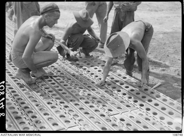 Members of No. 1 Airfield Construction Squadron, RAAF, laying sections of Marsden Mat during the rebuilding of the airstrip.