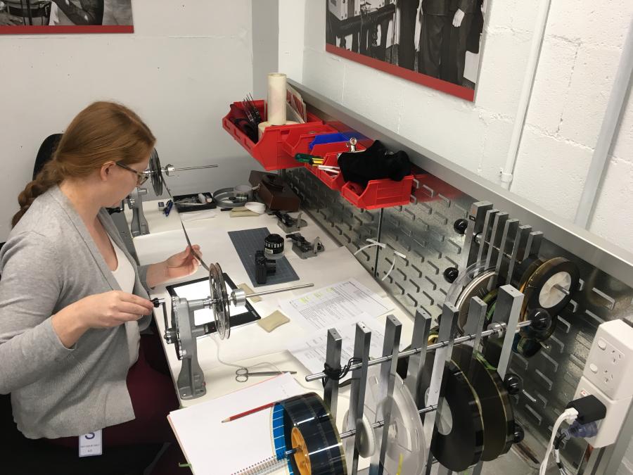 Caption: Conservator Maree Swann inspecting 8mm film on a manual film winding bench.