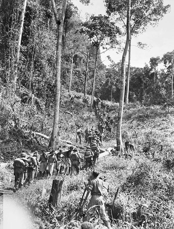 Native carriers and troops of the 2/9th Australian Infantry Battalion moving along the Kokoda trail in the Owen Stanley ranges during the filming of sequences for the production, "Rats of Tobruk" by Mr George Heath.