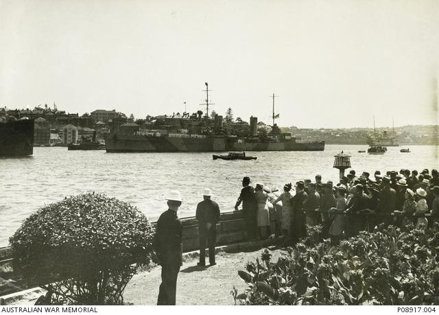 The crew of HMAS Sydney line the decks as they are greeted by a large crowd on the harbour foreshore. 