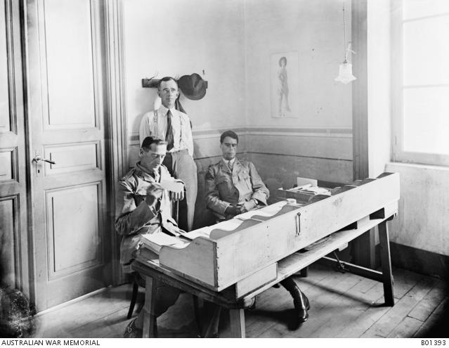 Two men sitting at a table, with one man standing in the centre behind them