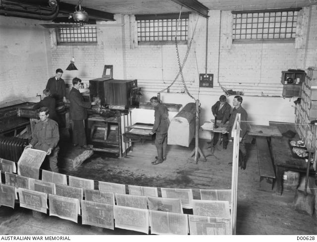 Newspapers hanging on three lines with men working in the background on the printing