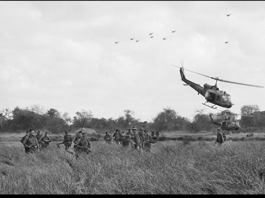 This photograph shows RAAF and American helicopters in the sky and swooping over a rice paddy in South Vietnam as they land troops of the 6th Battalion